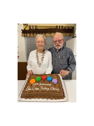 Couple standing by cake that reads "50th Anniversary, San Diego Rolling Homes"